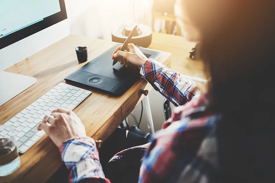 Young hipster girl sitting at her workspace and using modern computer and digital graphic tablet while working at vintage loft, professional female graphic designer or artist working at home , flare light, film effects